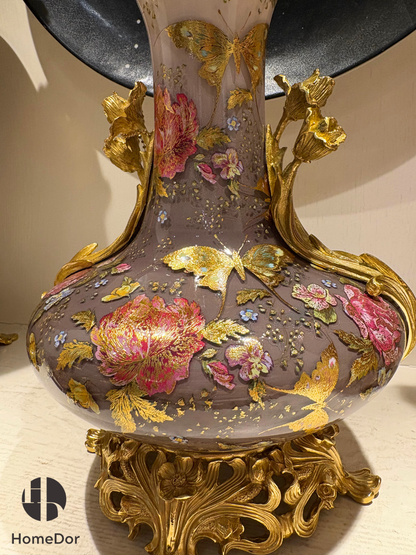 Comprising a monumental amphora, a decorative vase, and a decorative casket, the collection showcases a remarkable interplay of layered glass, gilded ornament, and floral artistry. Veils of smoky mauve, pearl-white, and soft gold create an ethereal backdrop for blooming peonies, delicate butterflies, and shimmering botanical motifs, lending each piece an extraordinary sense of depth and atmosphere.