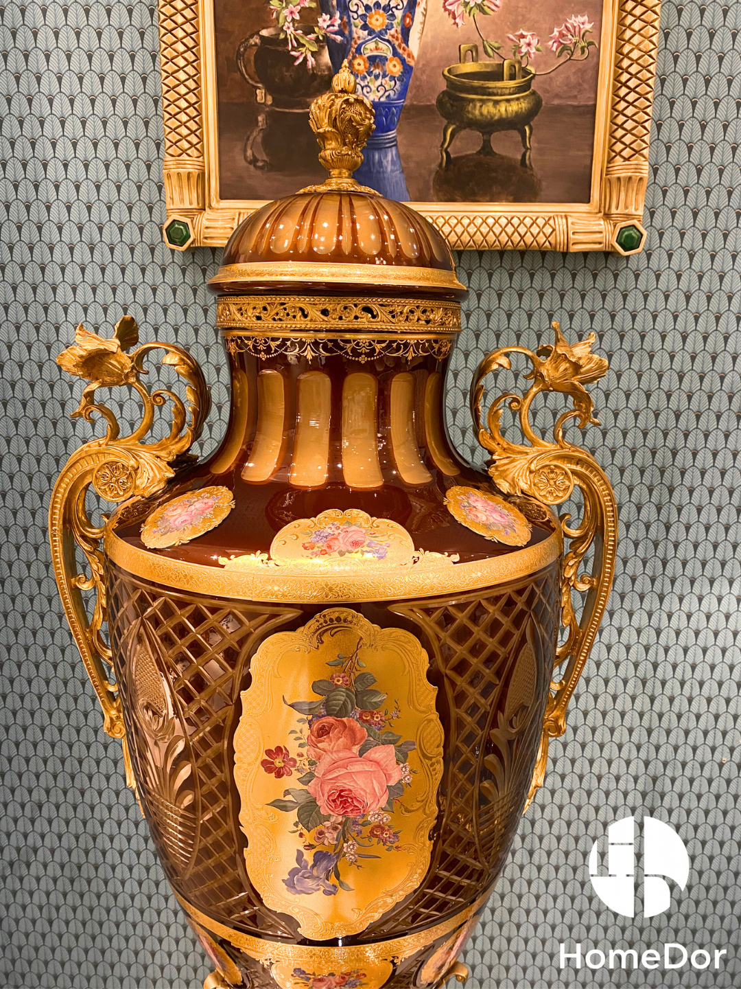 Crowned by a richly ornamented domed lid and framed by elaborate ormolu-style handles, the urn is adorned with hand-painted floral medallions set against a luminous amber-toned ground. Delicate latticework, gilded detailing, and jewel-like decoration enrich every surface, creating layers of visual depth that reveal new details from every angle.