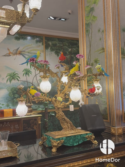 a masterpiece that blends opulent craftsmanship with vibrant artistic detail. Featuring vividly colored parrots and blooming florals perched on an intricately sculpted bronze tree, this lamp is adorned with crystal-encrusted lanterns and set atop a malachite-inspired base.Crafted from copper, high-temperature porcelain, and malachite accents, it exudes a sense of royal elegance, making it a focal point in living rooms, bedrooms, or luxury lounges. 